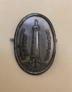 oval metal pin with monument at center. 