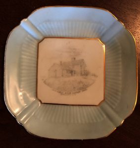 Lobed ceramic plate with image of a house at center. 